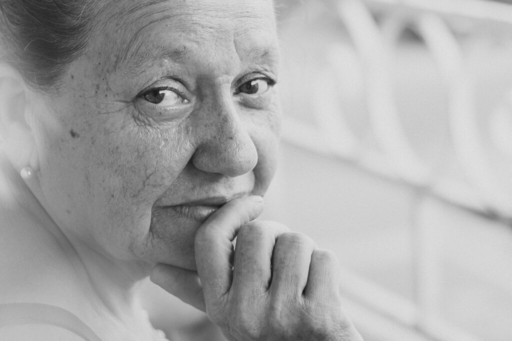 Close-up black and white portrait of a senior woman with a pensive expression, captured in soft lighting.